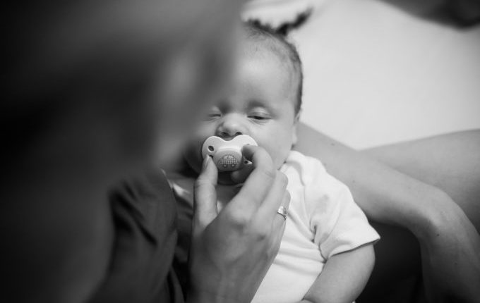 Baby im Arm eines Erwachsenen, der ihm einen Schnuller in den Mund drückt