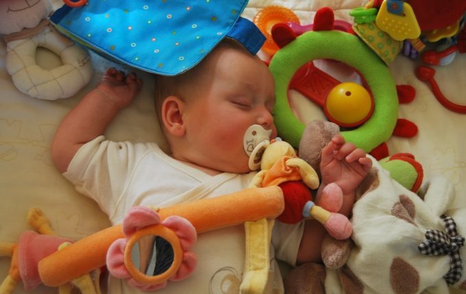 Baby schläft mit Schnuller im Mund umgeben von Spielzeug