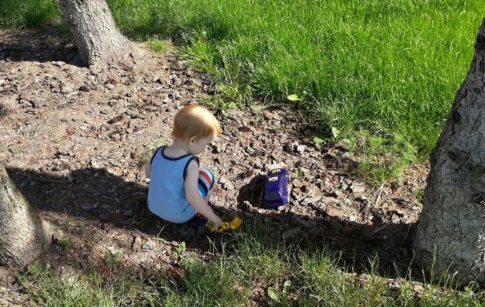 Sommertipps für Familien mit Baby und Kind - Kind spielt im Schatten eines Baumes mit Autos