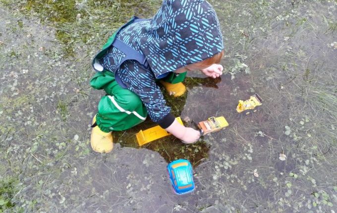 Kind spielt mit Autos in großer Regenpfütze