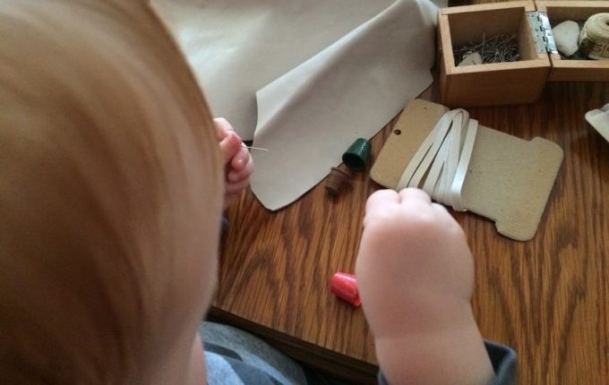 Das Indianerkostüm vom kleinen Mann - Kind spielt mit Nadel und Fingerhut