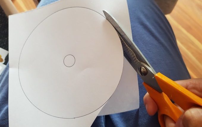 Hand schneidet CD Form auf Papier mit Schere aus