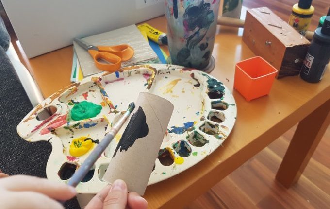 Kind malt Klopapierrolle mit Pinsel und Acrylfarbe an