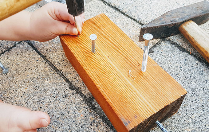 Kind schlägt Nagel mit Hammer in ein Stück Holz