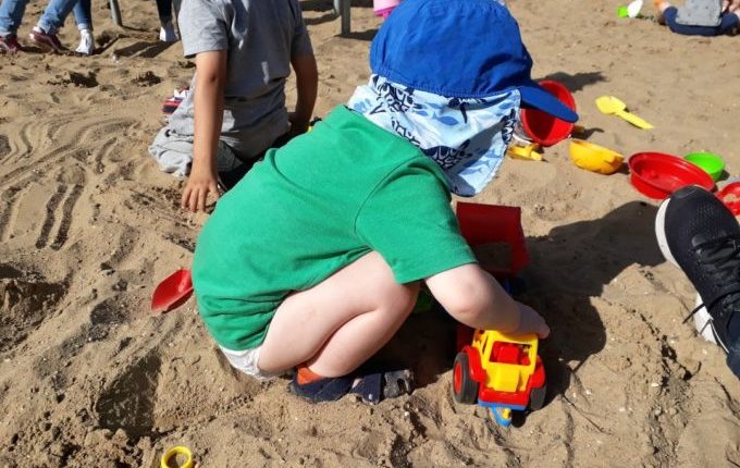 Kind spielt im Sandkasten mit fremdem Auto