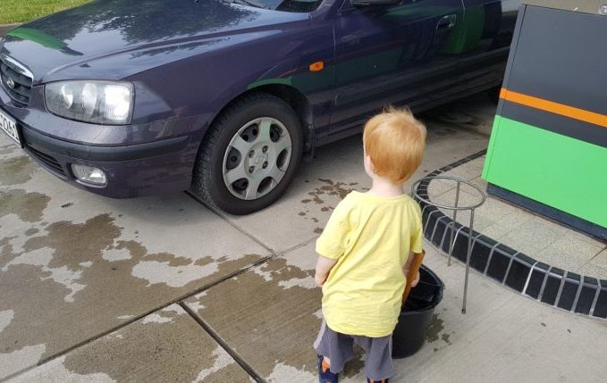 Kind wäscht Auto an der Tankstelle