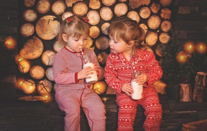 Kinder in Weihnachtskleidung trinken Milch aus Glasflaschen