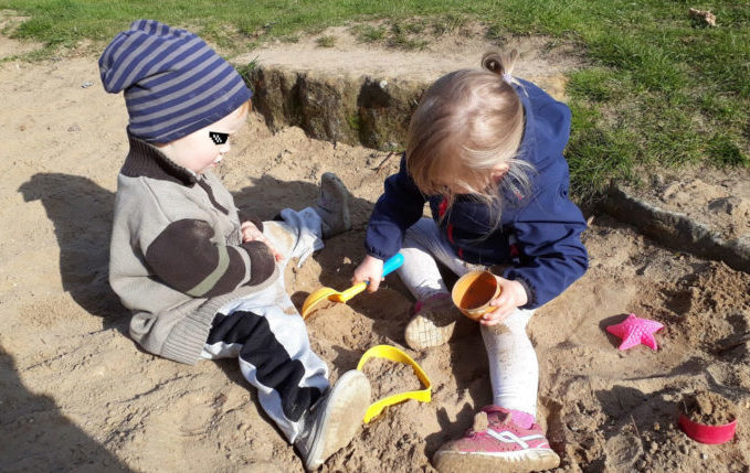 Kinder spielen gemeinsam im Sandkasten mit Buddelzeug