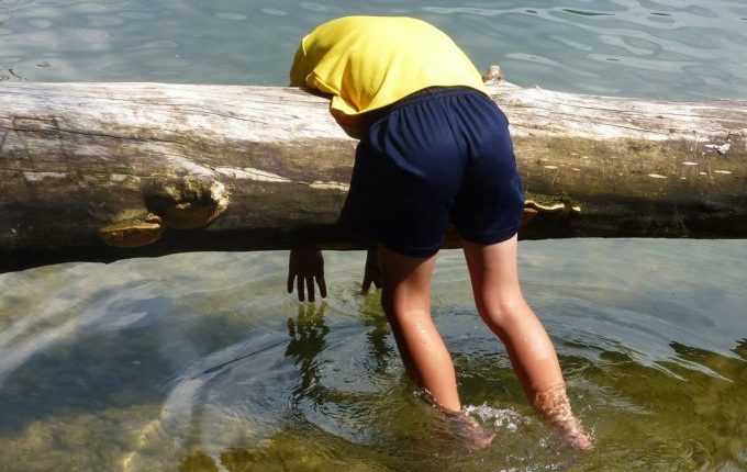 Mensch hängt schlapp über einem Baumstamm im Wasser