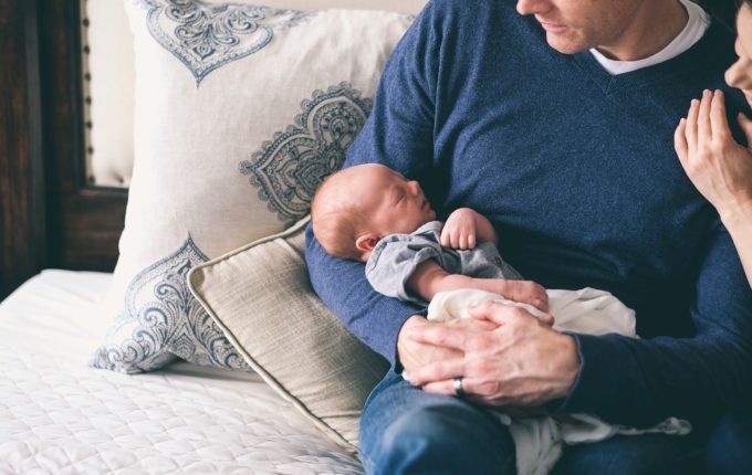 Mann hält schlafendes Baby im Arm, Frau freut sich