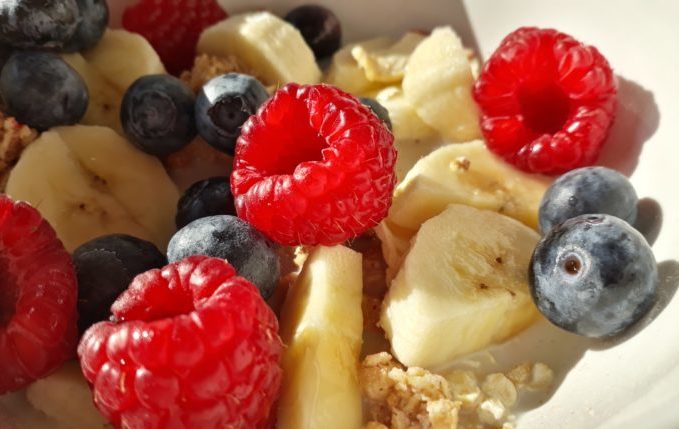 Müsli mit Haferflocken, Bananen, Blaubeeren, Himbeeren und Nüssen