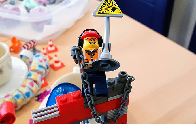 Legomännchen Bauarbeiter mit Warnschild auf der Baustelle