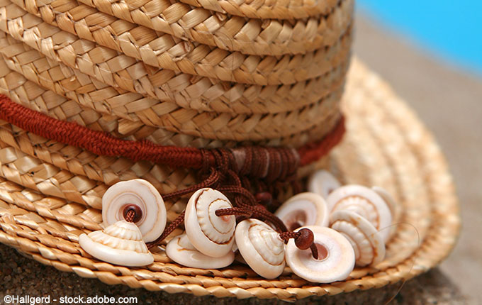 Strohhut mit rotem Band und Muscheln im Sand