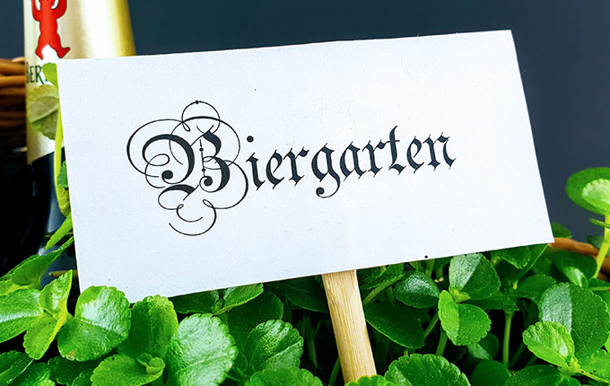 Biergartenschild im Korb umgeben von Pflanzen und Bier