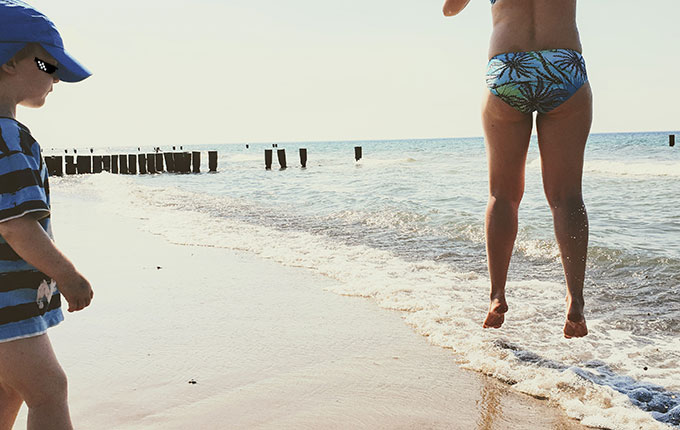 Frau springt am Strand über Welle