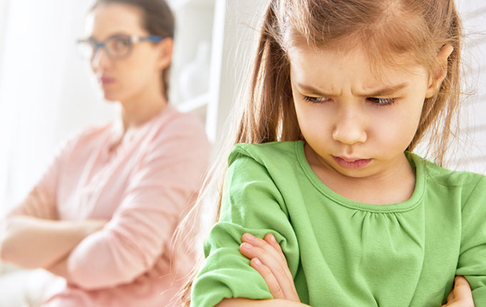 Kind schaut mit verschränkten Armen ärgerlich zu verärgerter Mutter