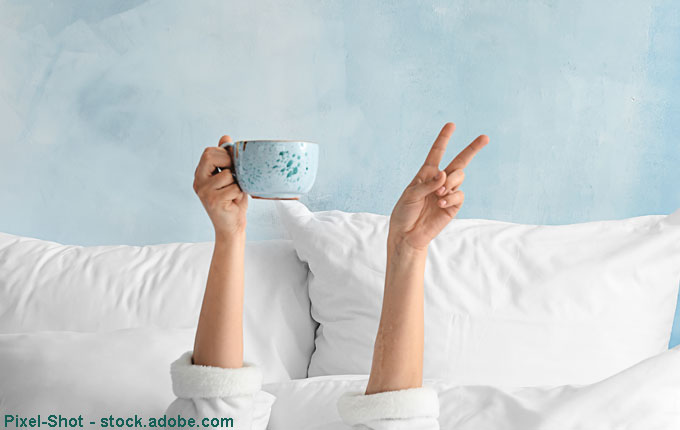 Hand hält Tasse im Bett hoch