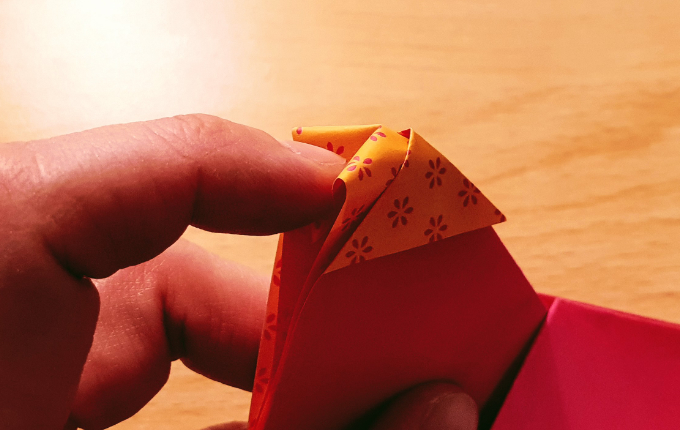 Finger knickt Spitze von Origami Huhn nach innen