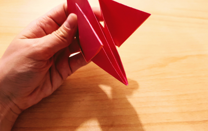 Hand hält Flügelschwanz von Origami Huhn fest