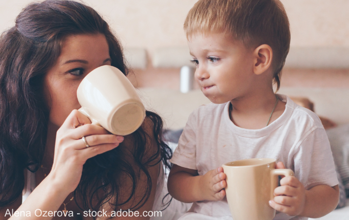 Mutter und Kind schauen sich an und trinken aus Tassen